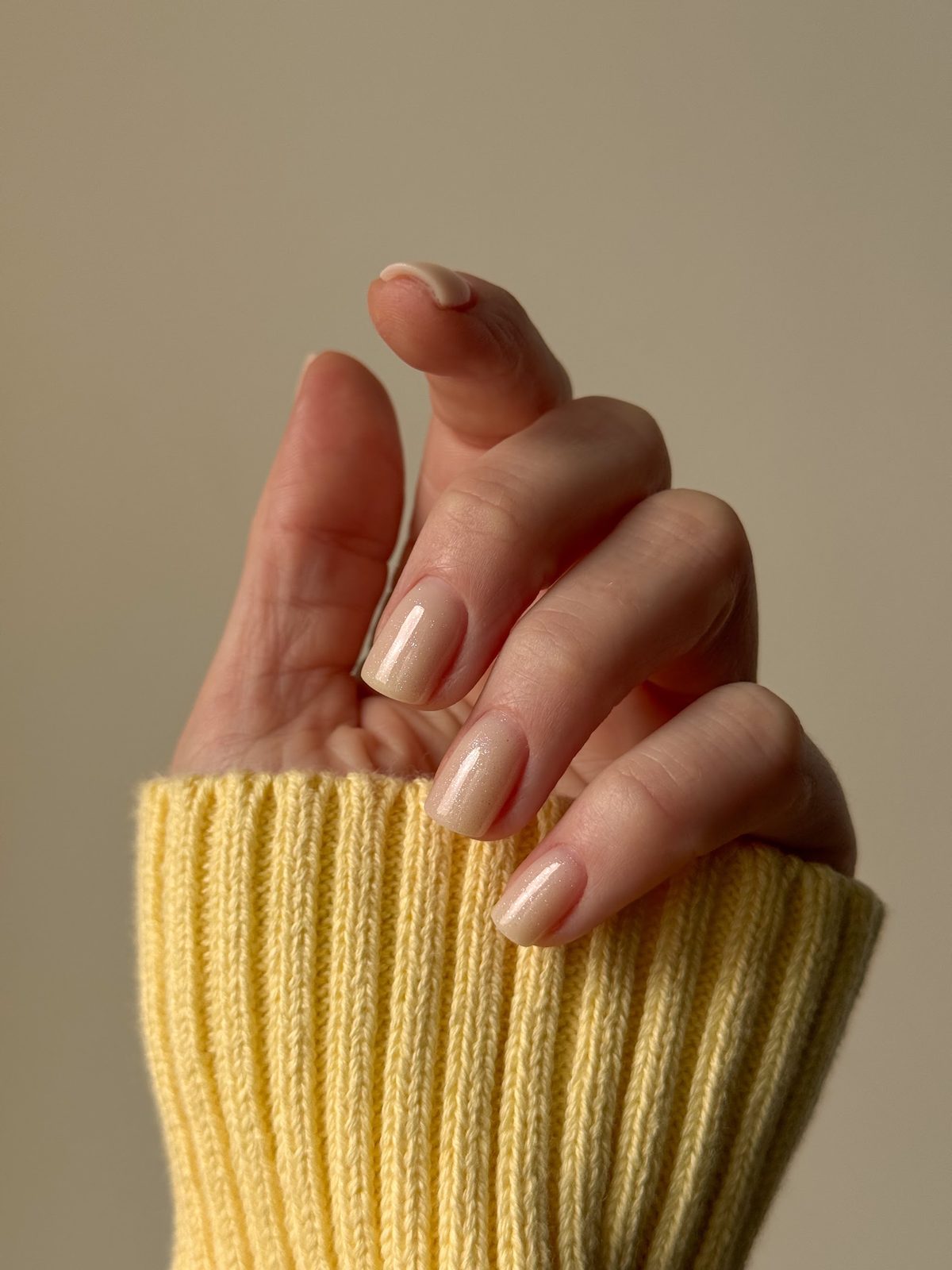 Nude nagels, de hand steekt uit een gele gebreide mouw