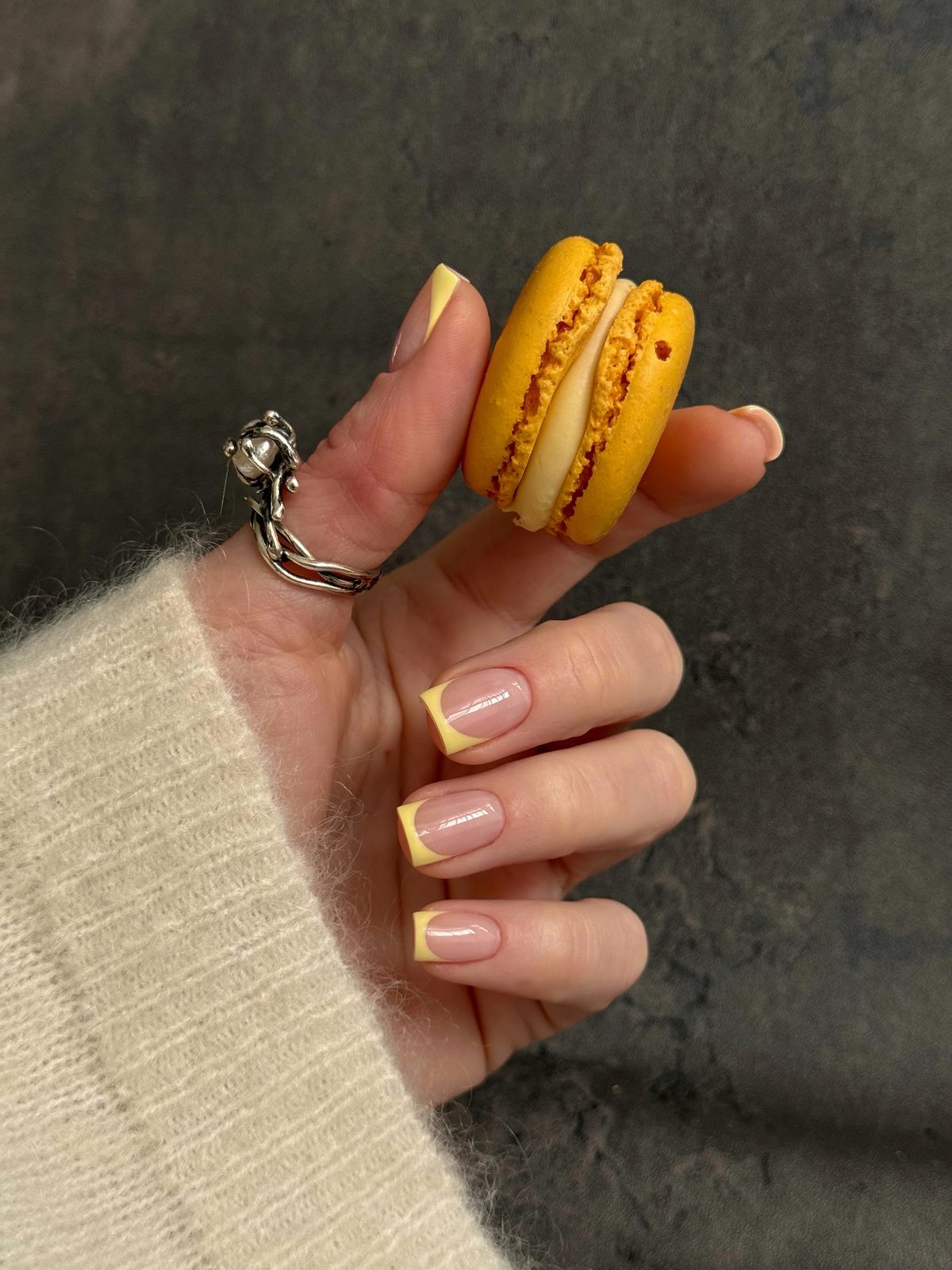 Nagels met een gele french, de hand houdt een gele macaron vast